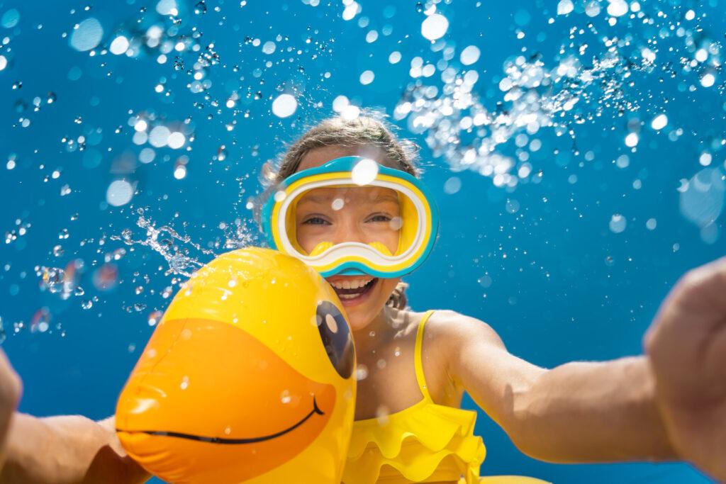 Glückliches Kind, das mit Taucherbrille und Schwimmreifen in Pool springt.