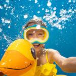 Glückliches Kind, das mit Taucherbrille und Schwimmreifen in Pool springt.