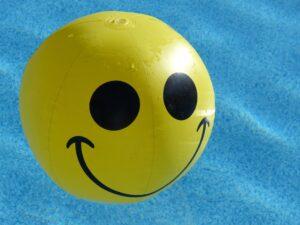 Gelber Wasserball mit lächelndem Gesicht, der im Pool schwimmt.