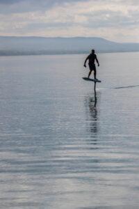 Mann, der mit einer Schwimmweste auf einem eFoil auf einem See fährt.
