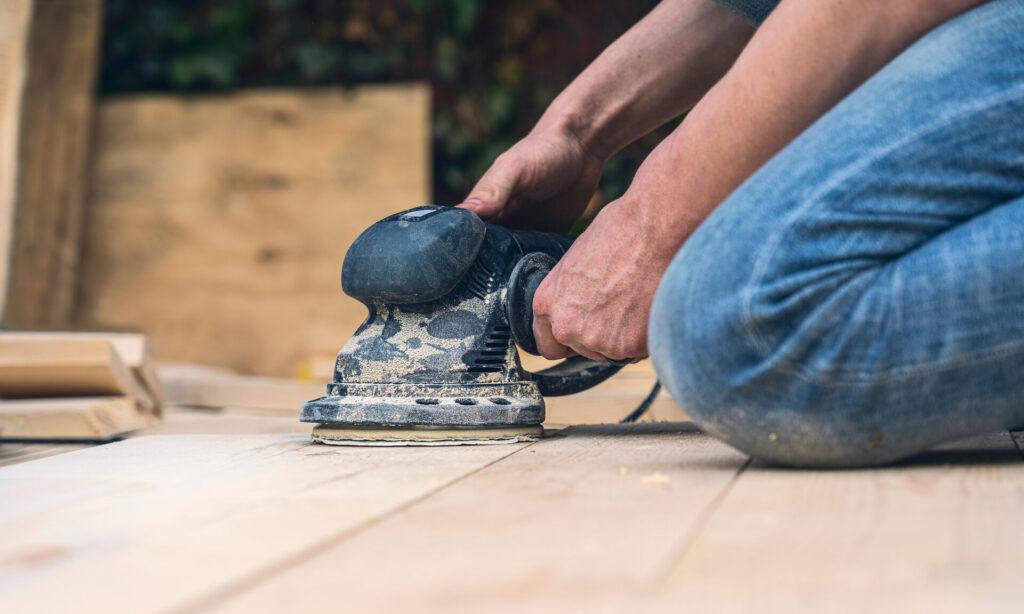 Nahaufnahme eines Arbeiters, der Holzbretter mit einer Schleifmaschine abschleift.