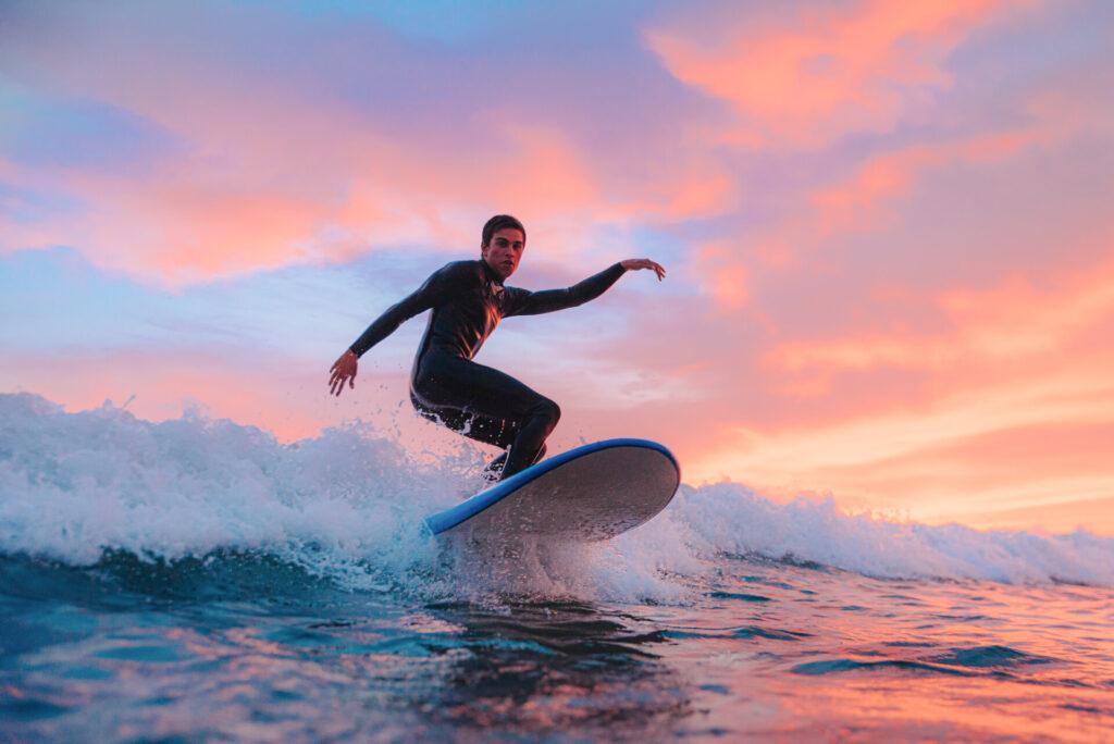 Junger Surfer, surft bei Sonnenuntergang an einem portugiesischen Strand.