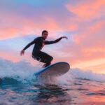 Junger Surfer, surft bei Sonnenuntergang an einem portugiesischen Strand.