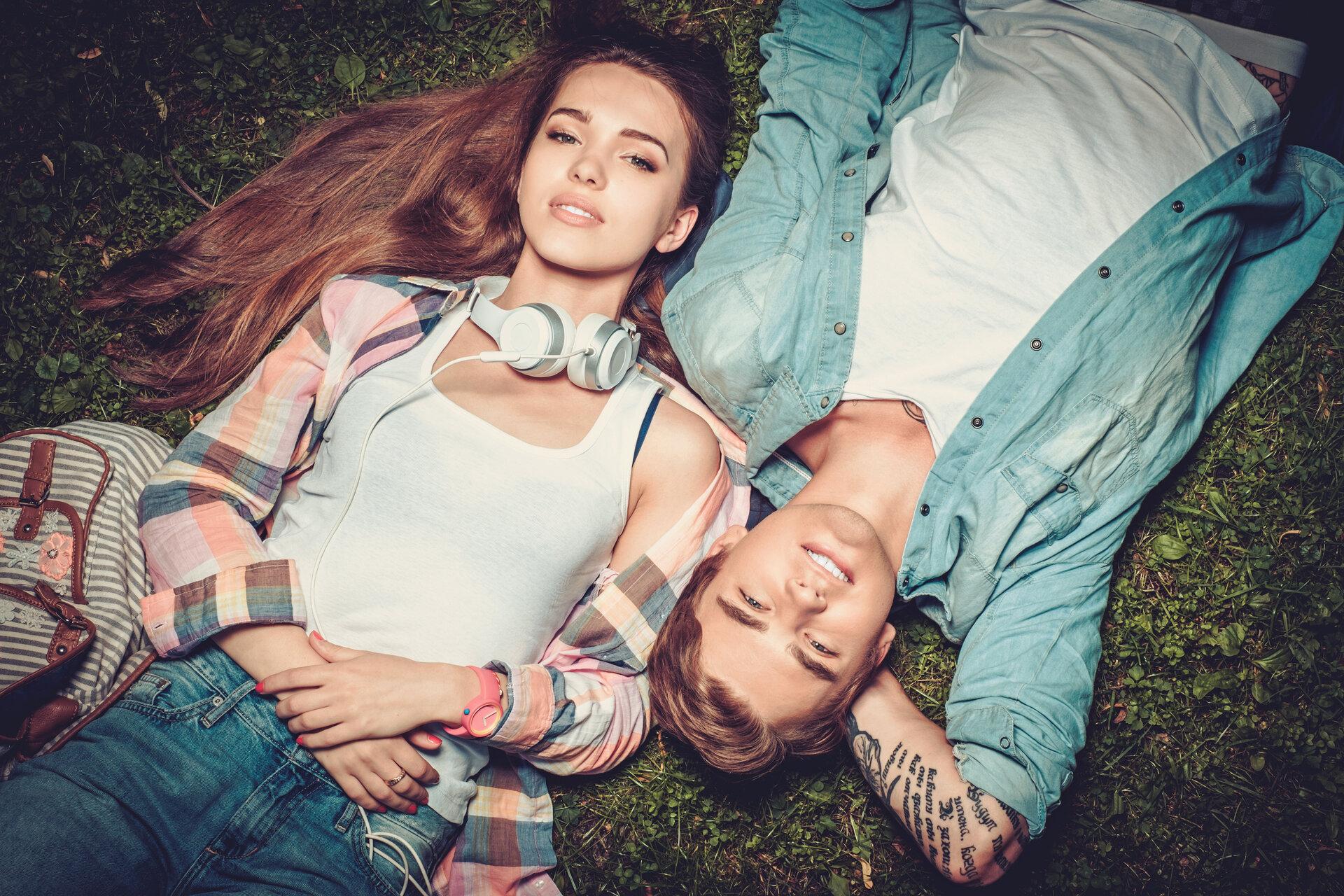 Fröhliches, junges Paar, mit stylischer Kleidung, das sich im grünen Park auf dem Boden ausruht.