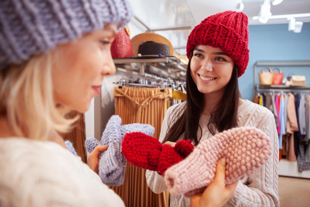 Freundinnen, die zusammen im Bekleidungsgeschäft einkaufen, sie probieren Wollmützen und Handschuhe aus