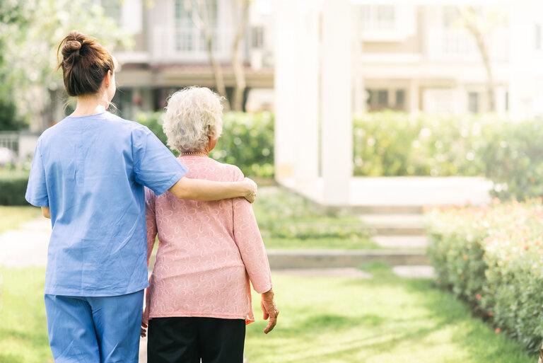 Rückenansicht der Krankenschwester Pflegekraft Unterstützung zu Fuß mit älteren Frau im Freien