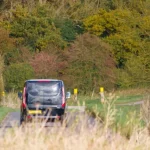Ein Ford Transit Custom fährt auf einer ländlichen Straße, umgeben von herbstlicher Natur, ideal für flexible Transportanforderungen.