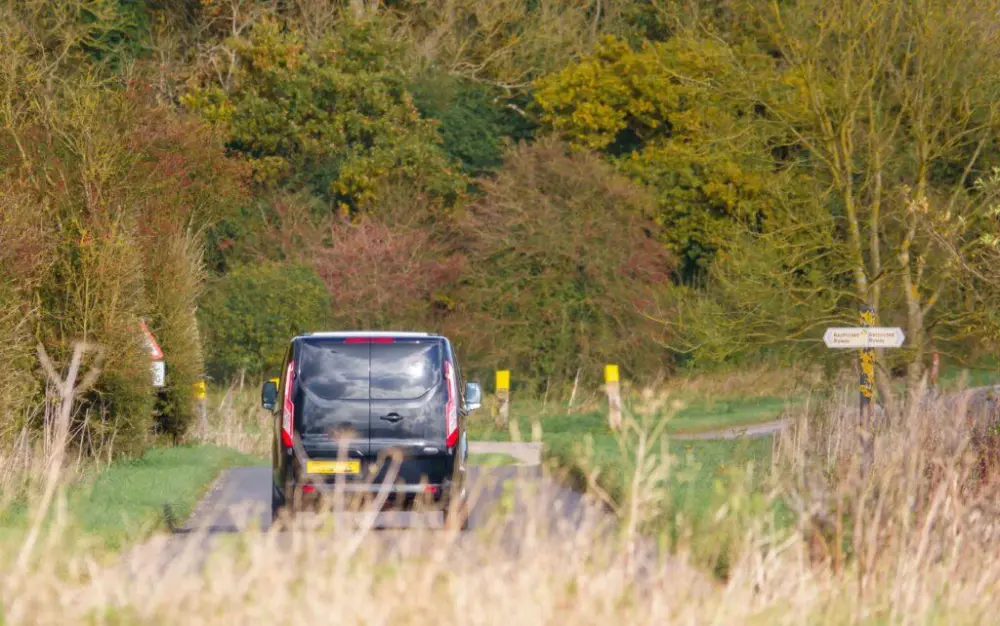 Ein Ford Transit Custom fährt auf einer ländlichen Straße, umgeben von herbstlicher Natur, ideal für flexible Transportanforderungen.